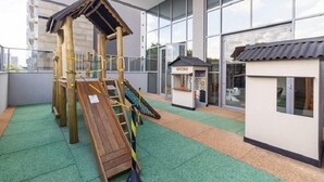 A children's play area with a slide, climbing structure, and small office building. - Helbor Wide (São Paulo)