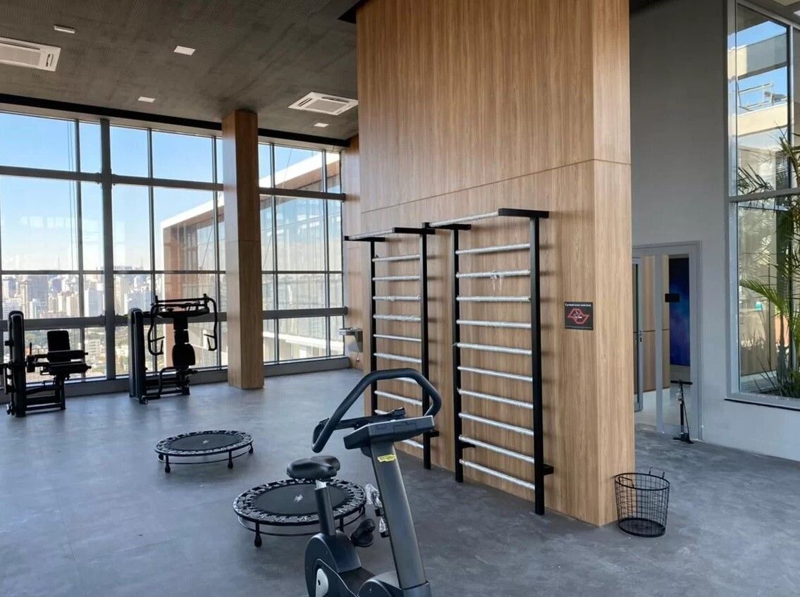 Ett gym med träningsutrustning, stora fönster och utsikt över staden.