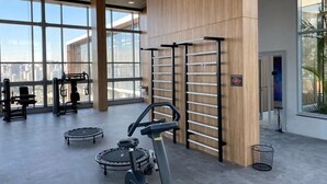 A gym with exercise equipment, large windows, and a view of the city. - Helbor Wide (São Paulo)