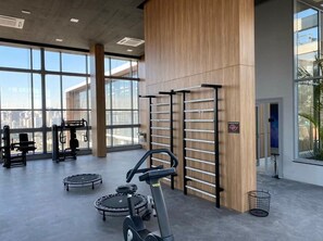 A gym with exercise equipment, large windows, and a view of the city. - Helbor Wide (São Paulo)