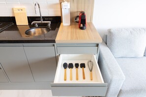 A kitchen with a sink, a coffee machine, and a drawer with kitchen utensils. - Helbor Wide (São Paulo)