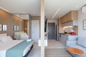 A modern hotel room with a bed, a sofa, a small table, a kitchen area, and a bathroom. - Helbor Wide (São Paulo)
