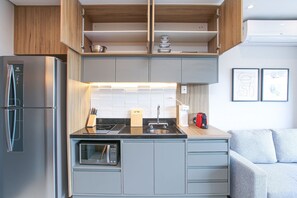 A compact kitchen with a built-in microwave, a stove, and a refrigerator. - Helbor Wide (São Paulo)