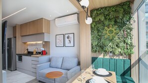 A modern kitchen with a built-in stove, a dining area with a table set for two, and a green wall with a sun decoration. - Helbor Wide (São Paulo)