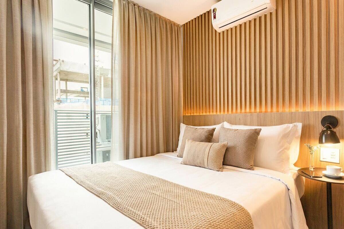 A hotel room with a large bed, a bedside table with a lamp, and a view of the outside.