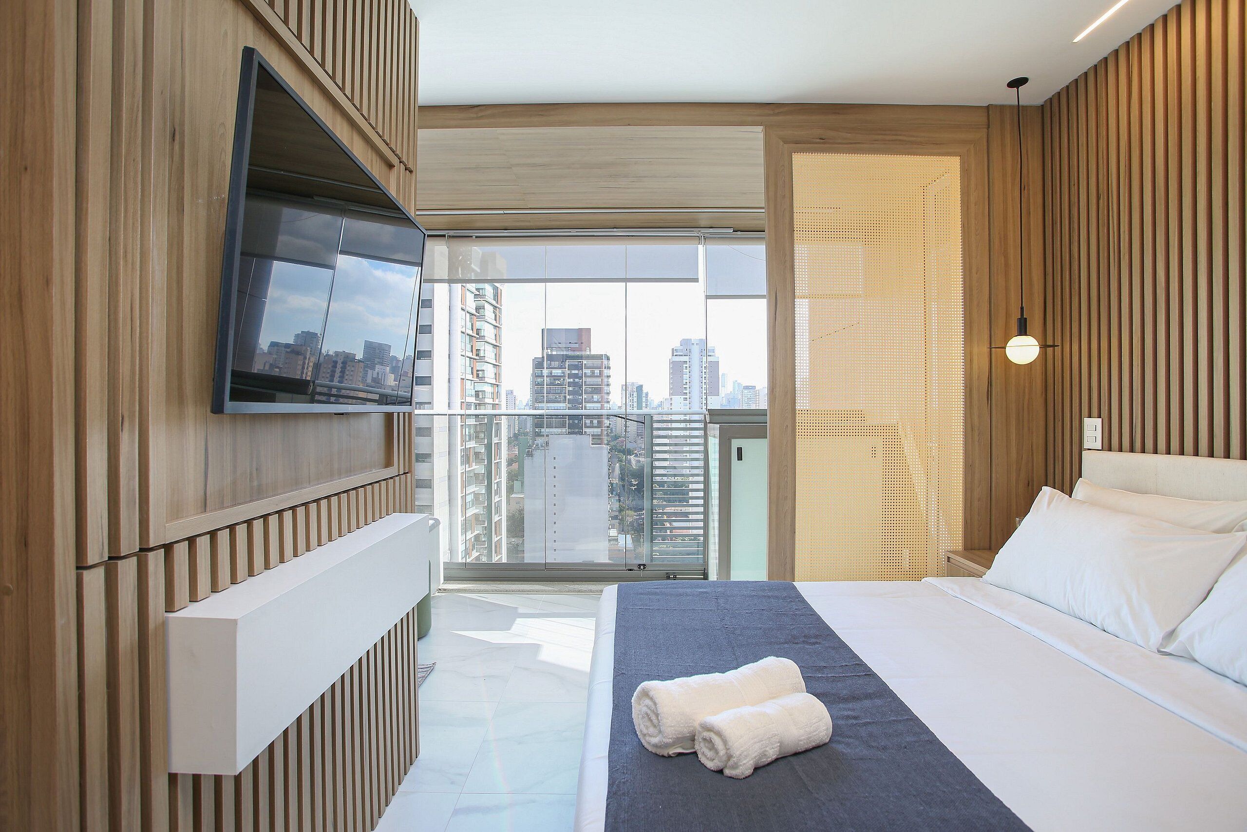 Habitación de hotel moderna con una cama grande, un televisor de pantalla plana, un balcón con vista a la ciudad y paneles de madera.