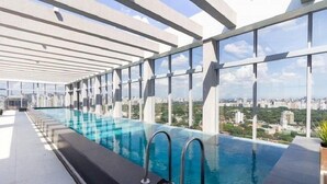 A rooftop infinity pool with a city view, enclosed by a white structure, and a clear sky. - Helbor Wide (São Paulo)