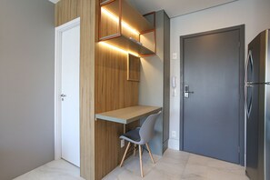 A compact room with a built-in desk, a chair, a door, and a refrigerator.