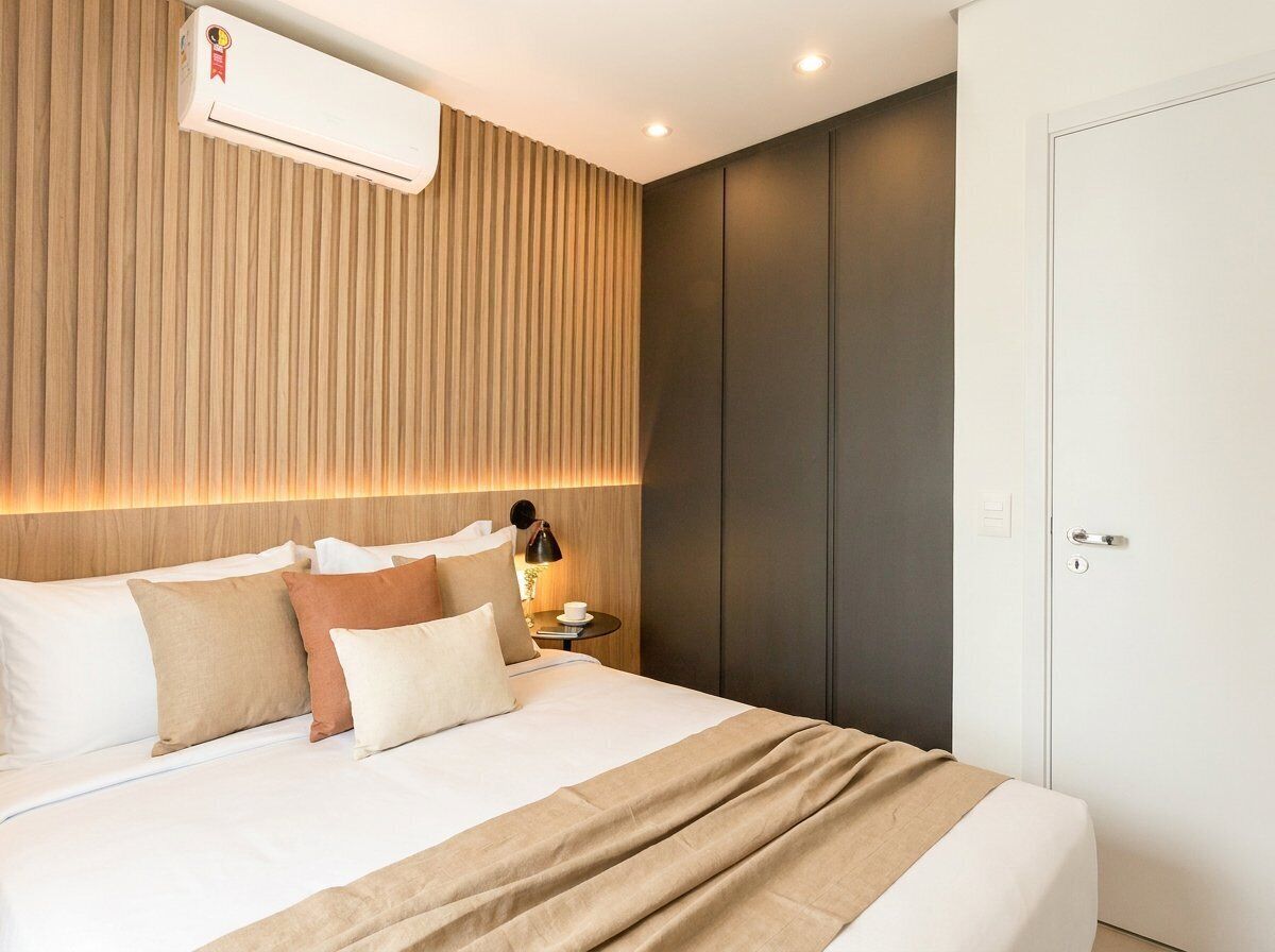 A modern hotel room with a bed, bedside table, lamp, and a wall-mounted air conditioner.