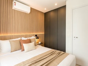 A modern hotel room with a bed, bedside table, lamp, and a wall-mounted air conditioner.