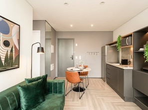 A modern kitchen with a dining area, a green sofa, and a minimalist design. - Helbor Wide (São Paulo)