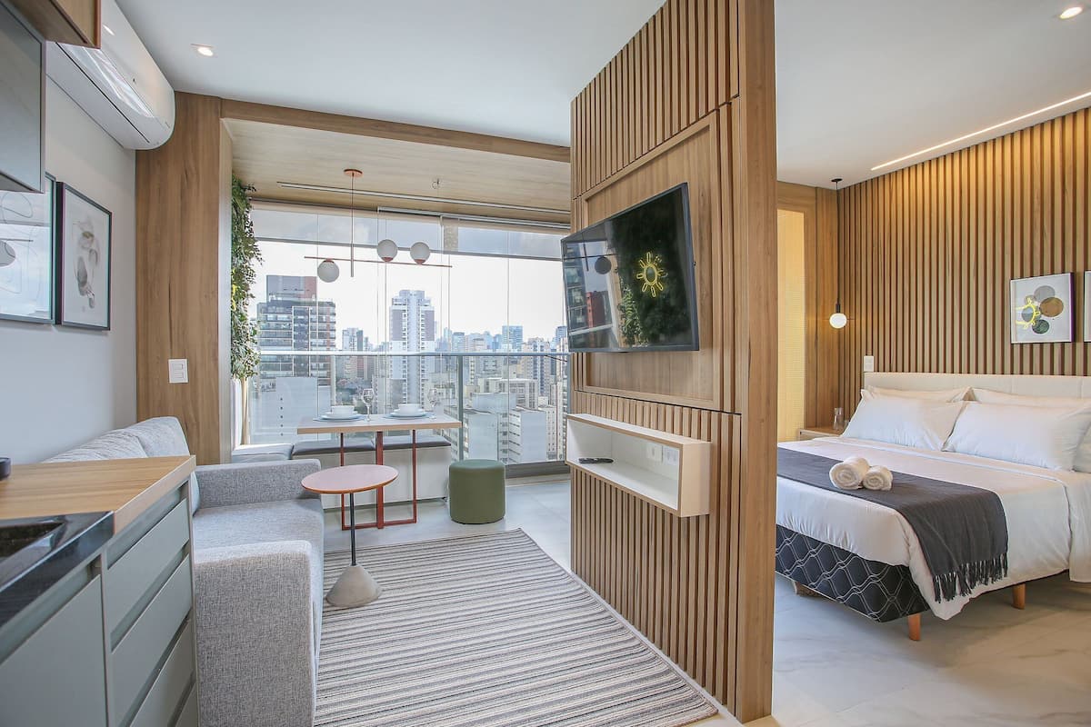 A modern hotel room with a city view, a bed, a desk, and a seating area.