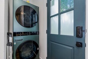 A front view of a laundry room with two stacked front-loading washing machines and a blue door with a window.