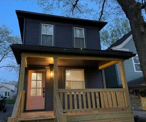 A two-story house with a front porch, a door, and a window with blinds.