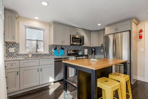 A modern kitchen with grey cabinets, a wooden island, stainless steel appliances, and a window. - Work & Relax in KC: Comfortable 2nd Floor Apt (2BR/2BA)| Near Plaza (Kansas City)