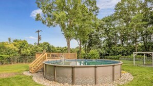 A circular hot tub with a wooden deck and steps, surrounded by a gravel border, in a grassy backyard with trees and a wooden pergola in the background. - 3 King Bedroom House with Pool in Charlott (Charlotte)