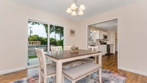 A dining area with a table, chairs, and a chandelier. There is a view of a patio with outdoor furniture and a tree. - 3 King Bedroom House with Pool in Charlott (Charlotte)