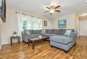 A living room with a sectional sofa, a coffee table, and a ceiling fan. - 3 King Bedroom House with Pool in Charlott (Charlotte)
