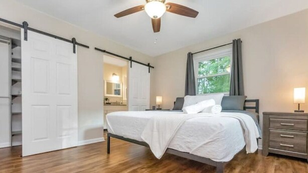 A bedroom with a bed, a ceiling fan, a nightstand, a dresser, and a sliding door leading to a closet. - 3 King Bedroom House with Pool in Charlott (Charlotte)