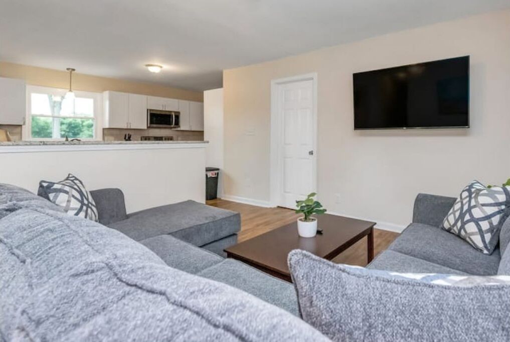 Ein modernes Wohnzimmer mit grauen Sofas, einem Couchtisch und einem an der Wand befestigten Fernseher.