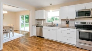 A modern kitchen with white cabinets, stainless steel appliances, and a wooden floor. - 3 King Bedroom House with Pool in Charlott (Charlotte)