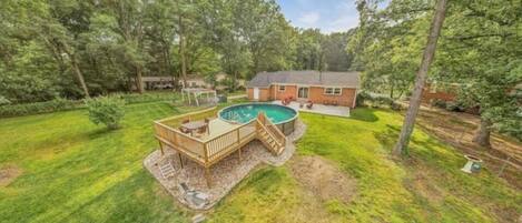 A backyard with a swimming pool, deck, and a house.