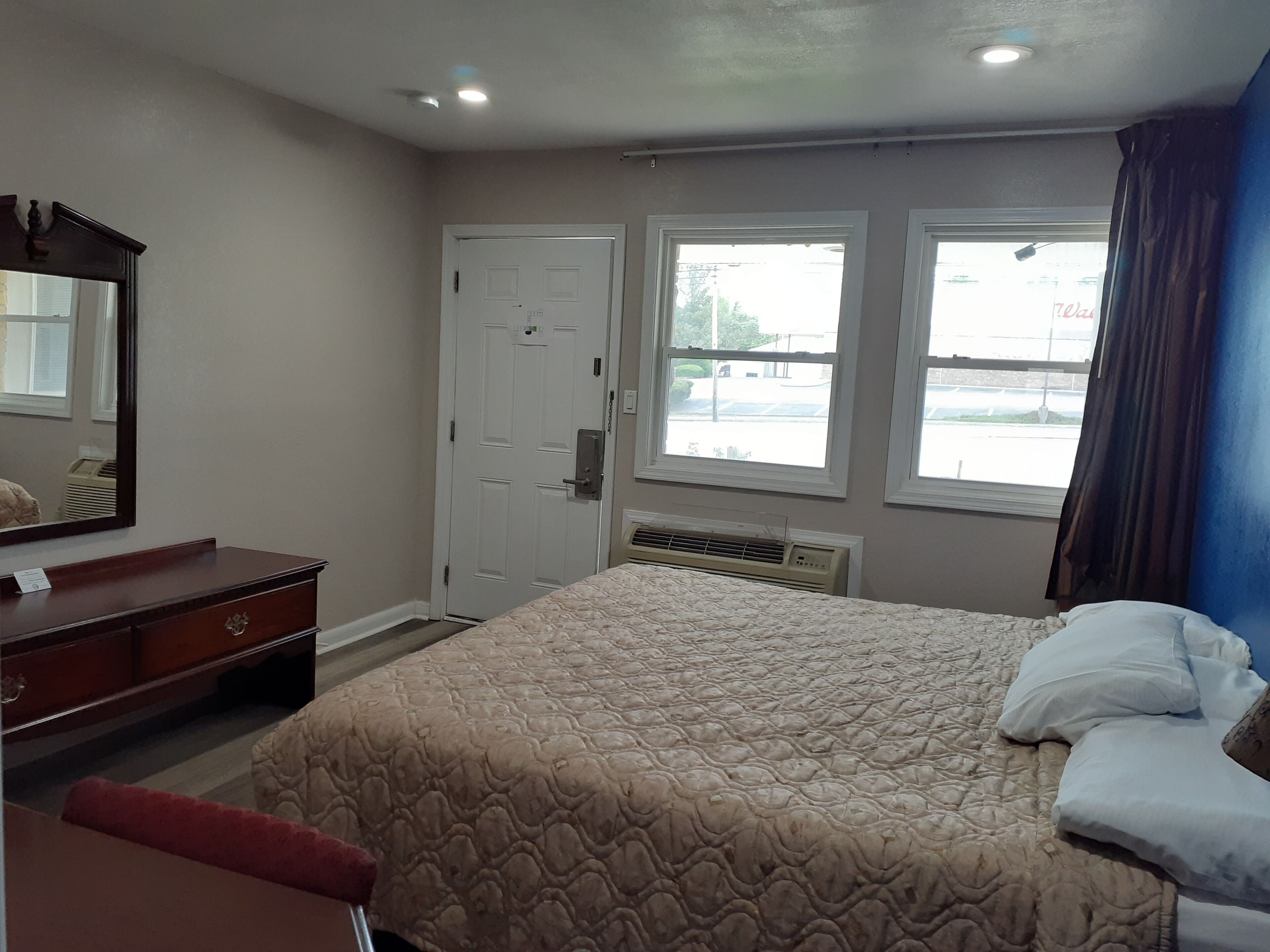 A bedroom with a bed, dresser, and two windows.