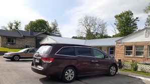 A maroon minivan parked in a driveway with a stone building and a white house in the background. - Scenic River Inn Wartburg Hwy 27 (Wartburg)
