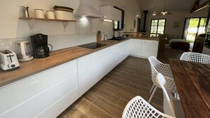 Una cocina moderna con armarios blancos, encimera de madera y estufa integrada. Hay un comedor con mesa de madera y sillas blancas.
