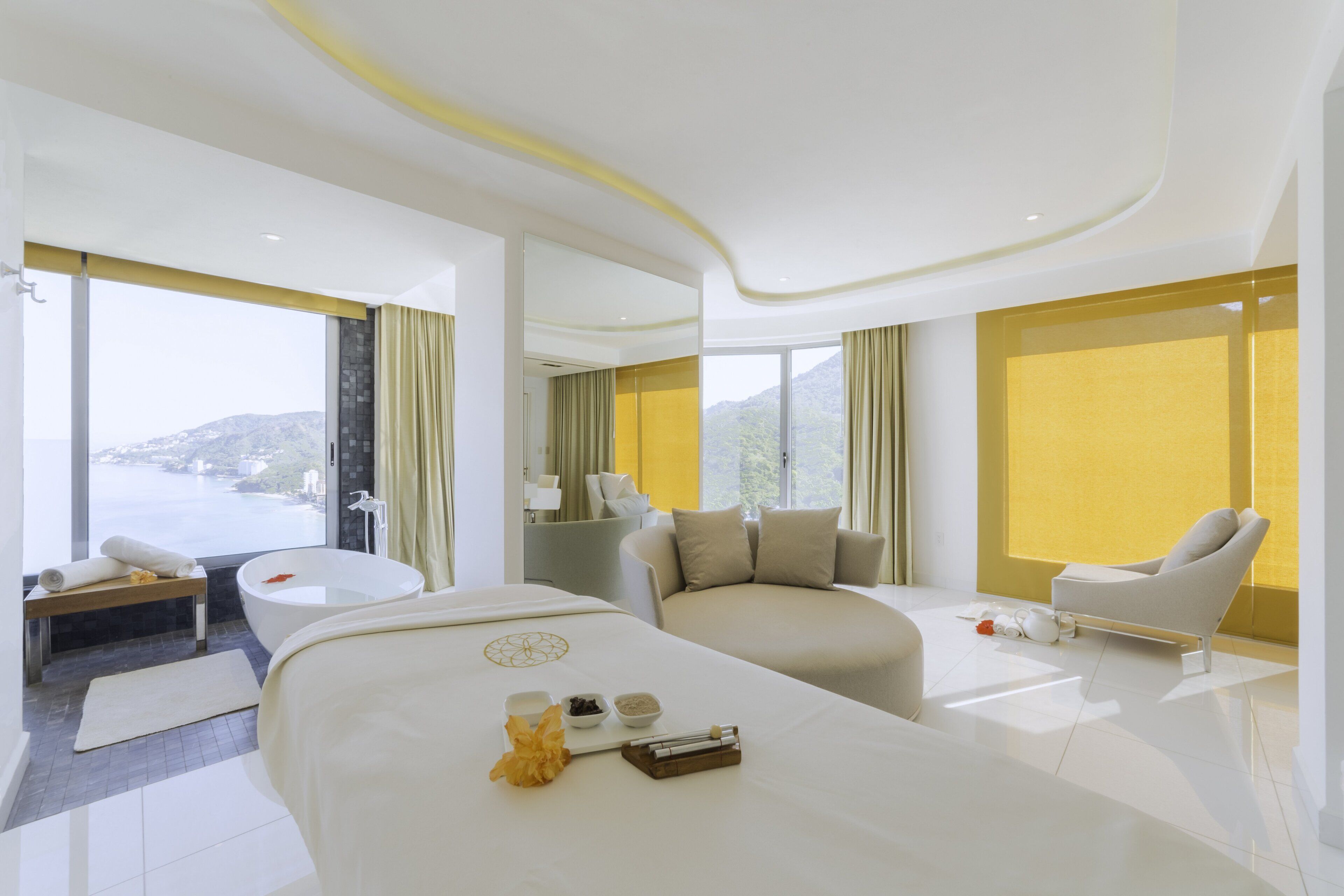 Habitación de hotel moderna con una cama grande, una zona de estar con una silla, una bañera y vistas a la montaña.