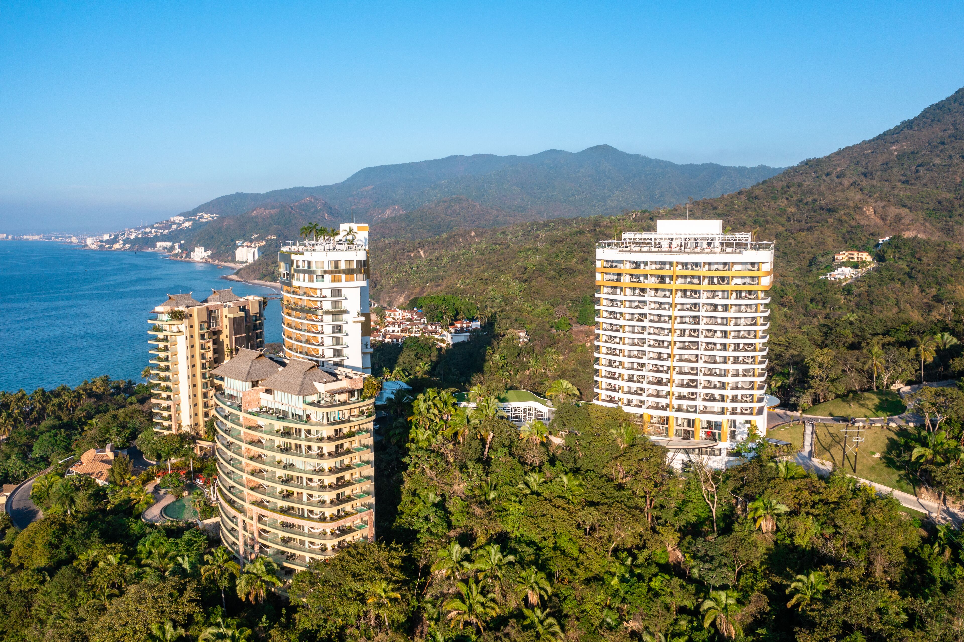 Un hôtel de grande hauteur doté de nombreux balcons, situé près d’une côte et offrant une vue sur un paysage montagneux.