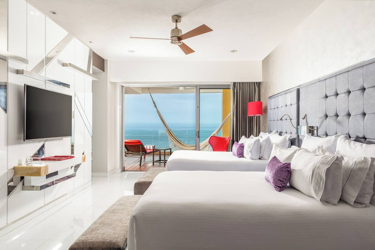 A modern hotel room with a large bed, a TV, and a view of the sea.