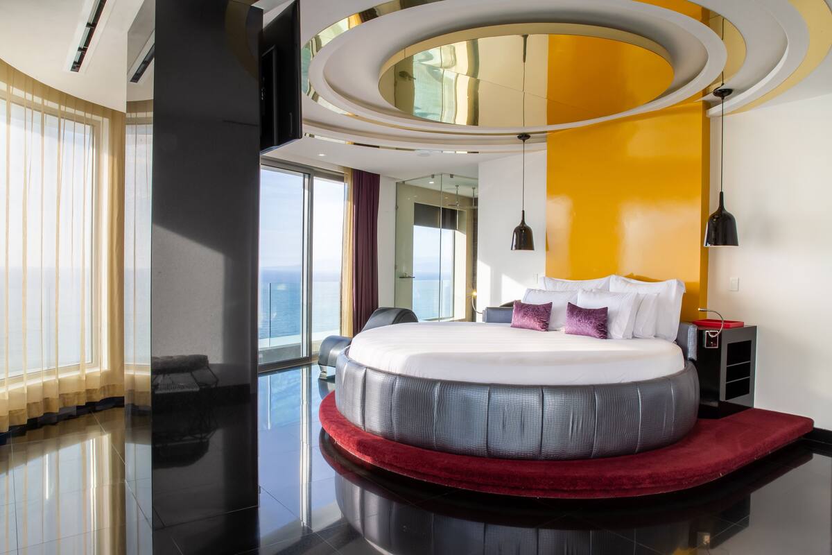 A modern hotel room with a circular bed, large windows, and a view of the city.
