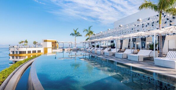 A poolside area with lounge chairs and umbrellas, overlooking a body of water. - Hotel Mousai Puerto Vallarta - All Inclusive - Adults Only (Puerto Vallarta)