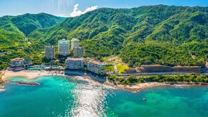 A coastal resort with multiple high-rise buildings, a beach, and lush green hills in the background. - Hotel Mousai Puerto Vallarta - All Inclusive - Adults Only (Puerto Vallarta)