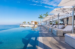 An infinity pool with clear blue water, lounge chairs, and umbrellas, overlooking the ocean. - Hotel Mousai Puerto Vallarta - All Inclusive - Adults Only (Puerto Vallarta)
