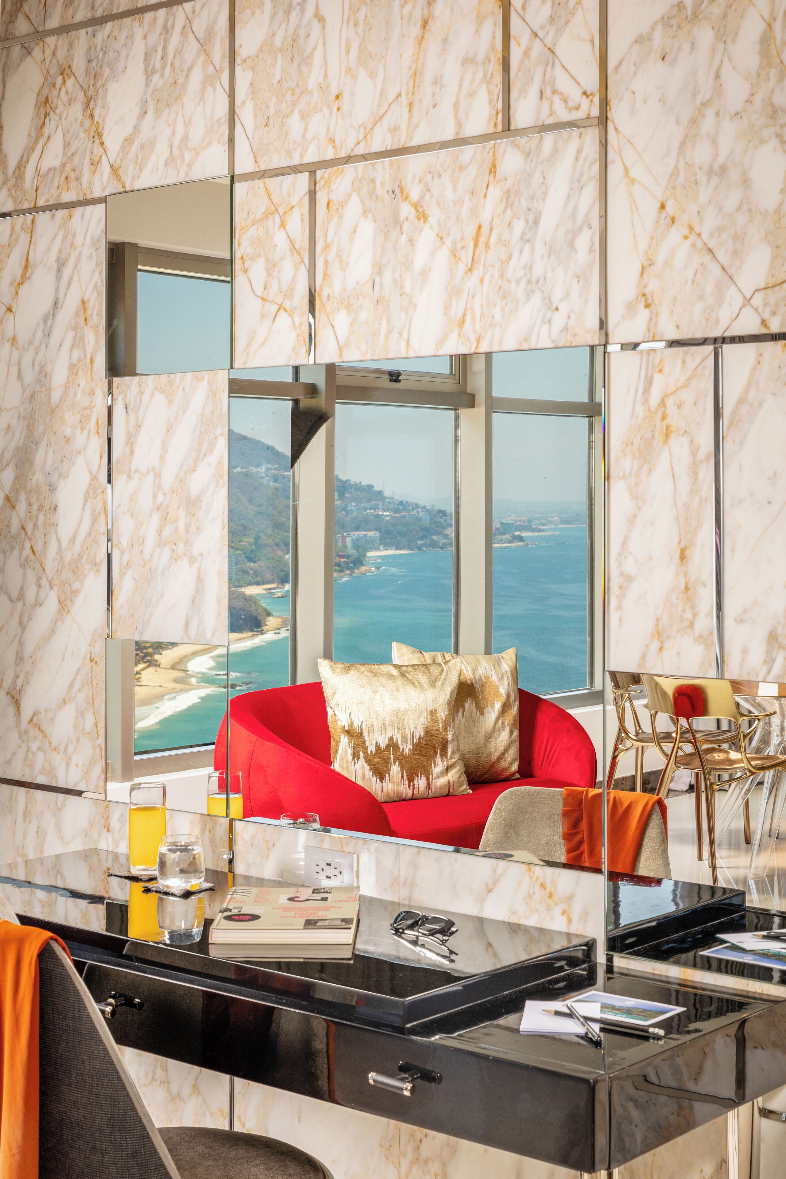Una habitación moderna con un espejo grande que refleja una vista panorámica del océano y las colinas.