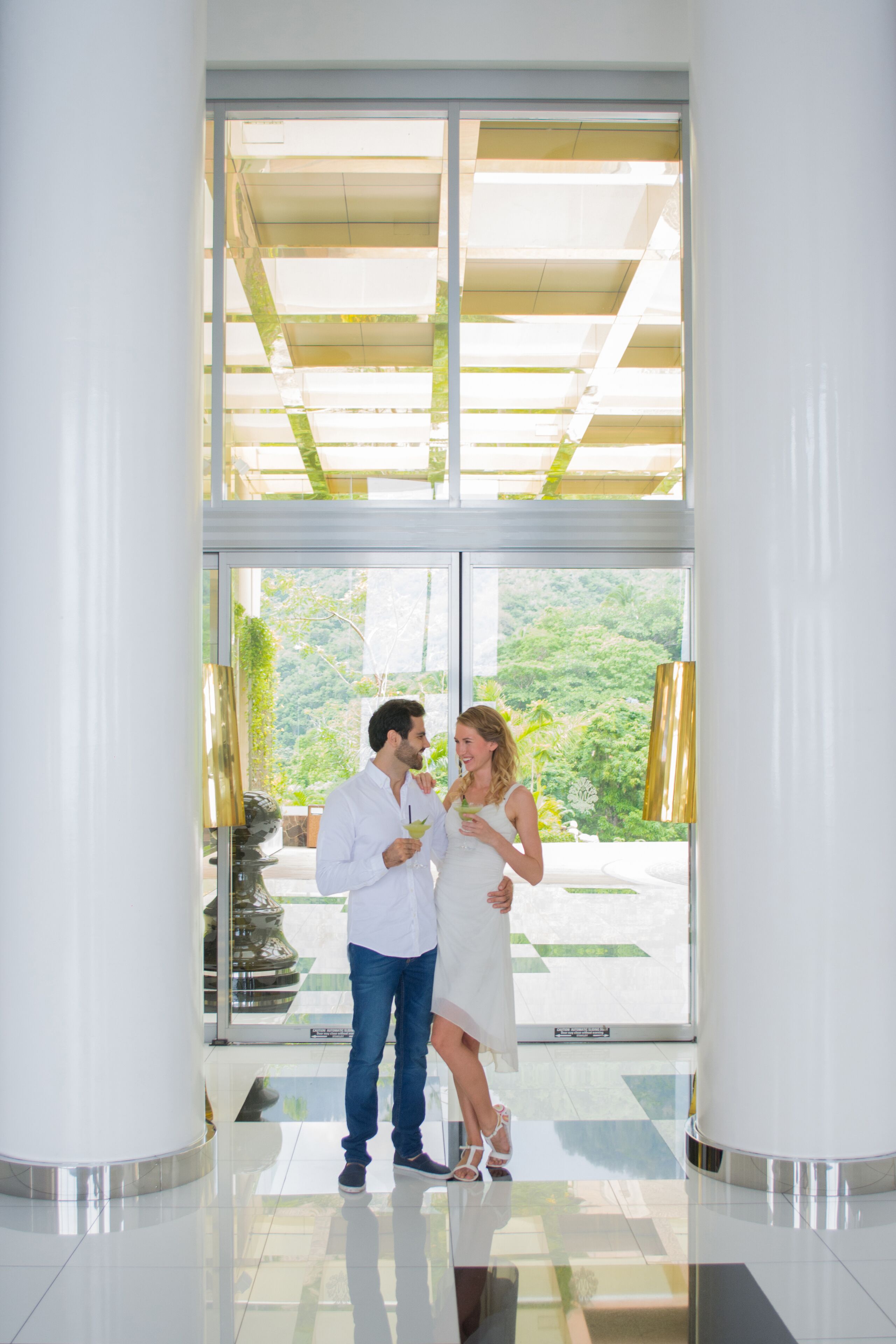 A couple standing in a modern lobby with large glass doors leading to a garden view.