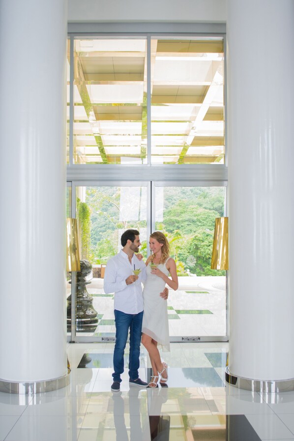 A couple standing in a modern lobby with large glass doors leading to a garden view.