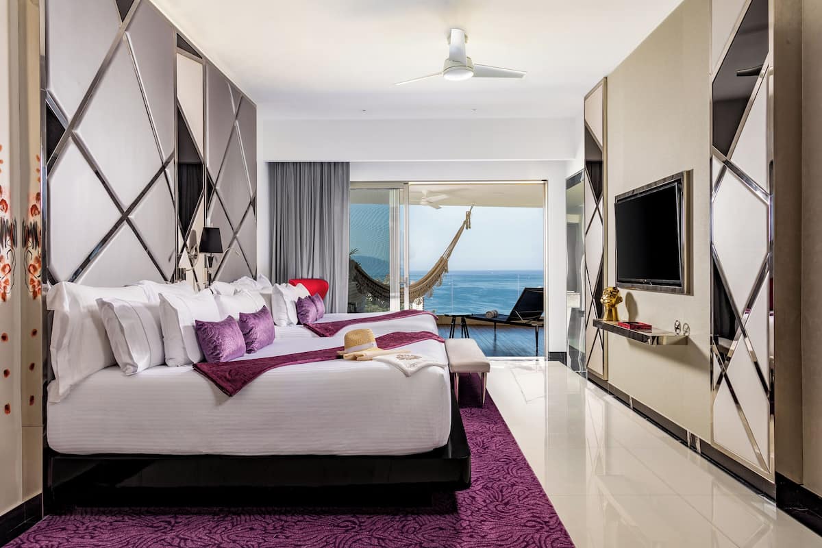 A modern hotel room with a large bed, a TV, and a view of the ocean.