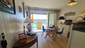 A cozy room with a wooden table, chairs, a lamp, and a view of the sea. - A Louer T2 Pour Trois Avec Piscine Dans la Résidence (ARZON)