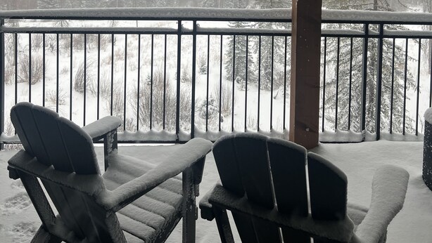 A covered outdoor area with two Adirondack chairs facing a snowy forest view. - Spectacular Mountain Retreat (Winter Park)
