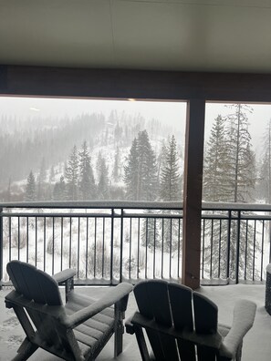 Un espace extérieur abrité, doté de deux fauteuils Adirondack donnant sur une forêt enneigée.