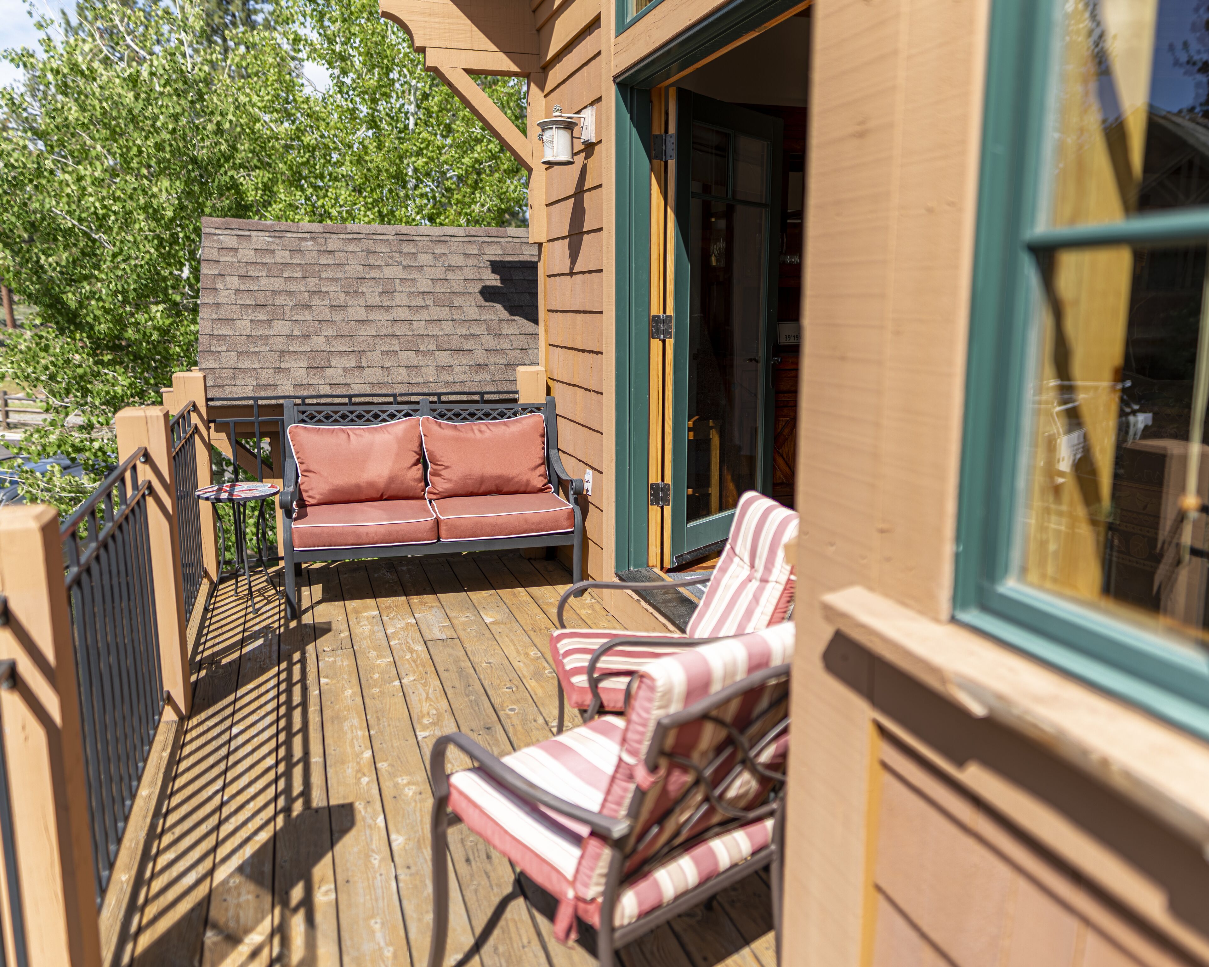A wooden deck with a sofa and striped chairs, a small table, and a window with a view of trees.