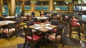 Un comedor amplio con altos techos de madera y un candelabro central. Las mesas están dispuestas alrededor de la sala, con sillas tapizadas en rojo y negro.