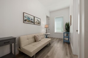Un salon moderne avec un canapé beige, une petite table avec une lampe et des œuvres d’art encadrées accrochées au mur.