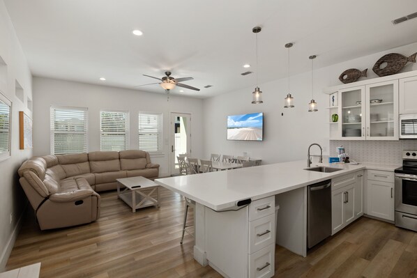 Una cocina moderna con armarios blancos, una isla central y una zona de comedor con un sofá color beige.