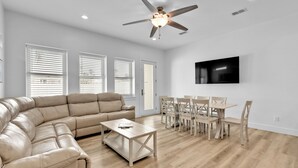A spacious living room with a beige sectional sofa, a wooden coffee table, and a dining area with wooden chairs and a table.
