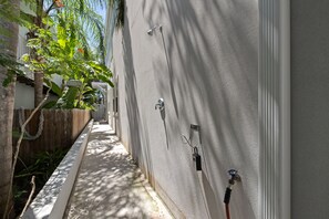 Un étroit sentier bordé d’un côté par un mur blanc et de l’autre par une clôture en bois, qui mène à l’entrée d’un bâtiment.