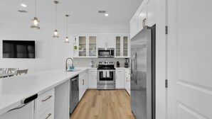 A modern kitchen with white cabinetry, stainless steel appliances, and pendant lighting.